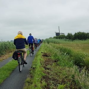 Radfahrer fahren auf einem schmalen Pfad an den Windmühlen von Kinderdijk vorbei